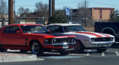 1972 Ford Ranchero - Two iconic American muscle cars, a red Ford Mustang and a white Chevrolet Camaro, are parked in a lot.