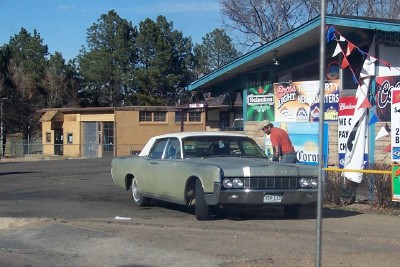 1972 Ford Ranchero - A man leans over the hood of a 1967 Lincoln Continental outside a store.