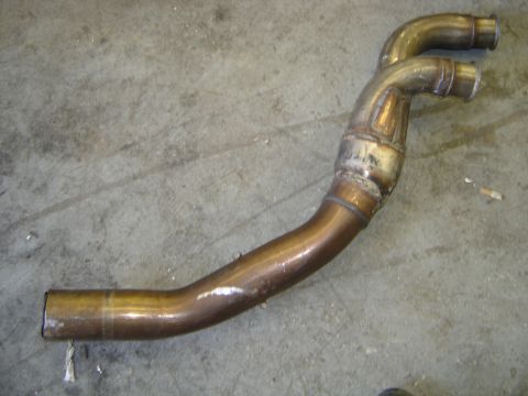 1997 Ford Ranger - A metal exhaust pipe with a Y-shaped configuration lies on a concrete surface.