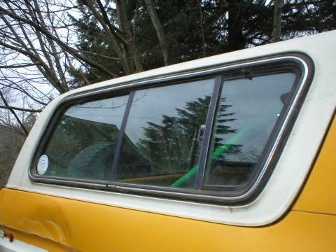 1978 Ford Bronco - A spare tire is visible through the rear quarter window of a yellow Ford Bronco with a white camper shell.