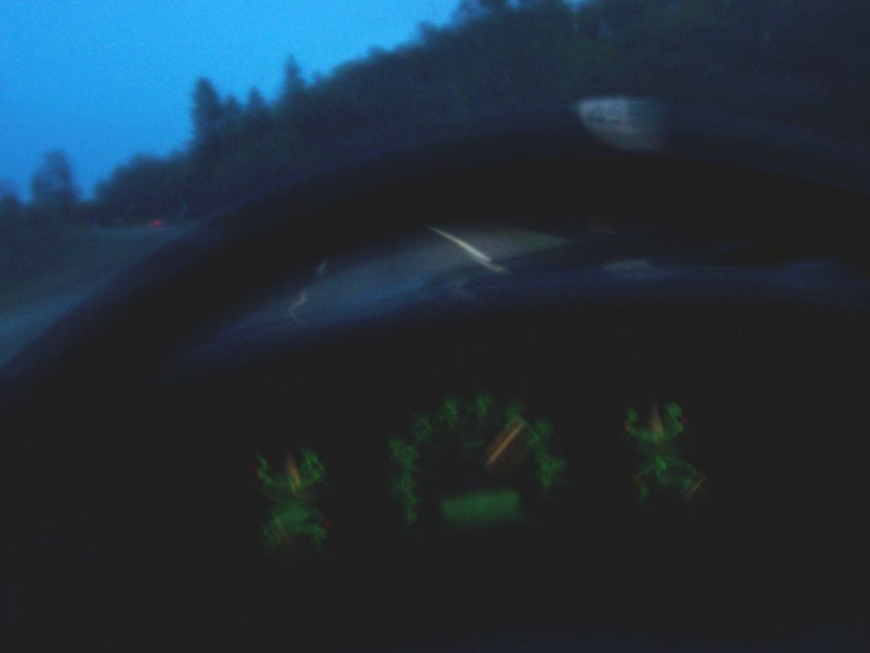 dashboard with glowing green gauges and a blurry road scene outside the windshield at dusk
