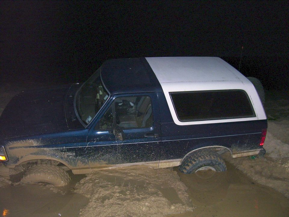 Blue and white 1992 Ford Bronco stuck in mud, side view