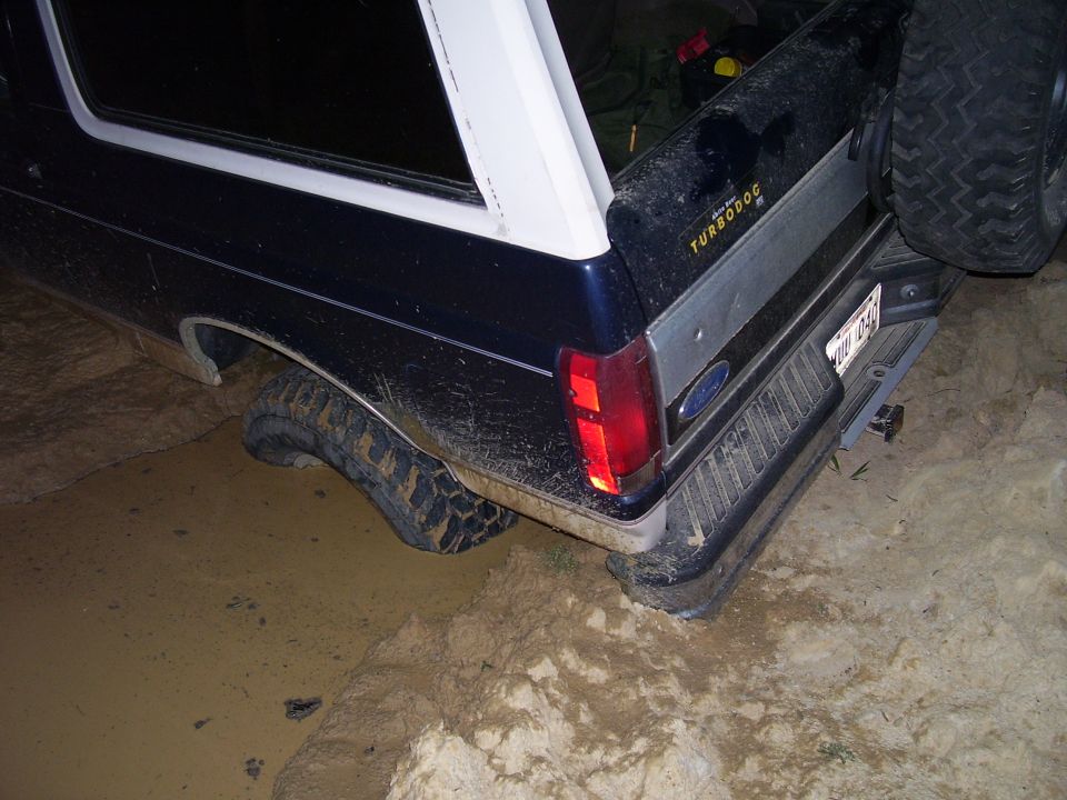 Dark blue 1992 Ford Bronco with white top stuck in mud, rear view