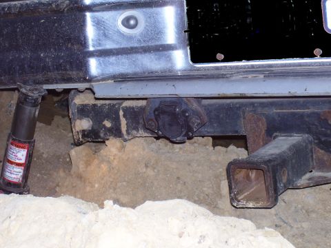 1992 Ford Bronco - Trailer hitch receiver and jack are visible under a vehicle's bumper, suggesting it is being worked on or is stuck.
