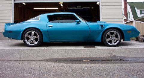 1979 Pontiac Trans Am - This blue coupe, likely a 1977 model, is shown from the side in front of a garage. It has custom chrome wheels.