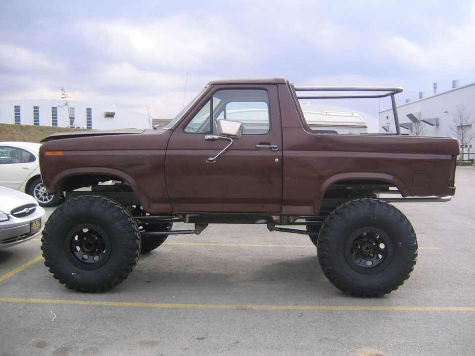 Lifted brown Ford Bronco with large tires, parked next to a white car