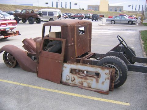 1978 Ford Bronco - A heavily rusted truck chassis sits in a parking lot, missing many of its body panels.