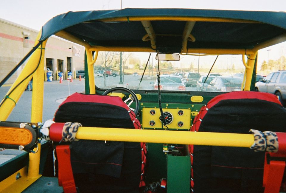 1976 Jeep CJ7 interior with green dash, yellow roll cage, and red/black seats. Aftermarket gauge cluster visible