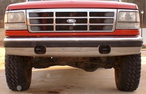 1995 Ford F-150 - The front grille and bumper of a red Ford F-150 truck are visible, along with its large tires.
