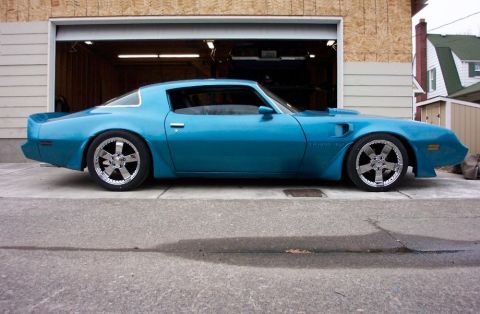 1979 Pontiac Trans Am - A blue 1979 Pontiac Trans Am with custom wheels is parked in front of a garage.