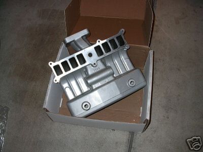 1991 Ford Bronco - A silver intake manifold is shown inside a cardboard box, resting on a concrete surface.