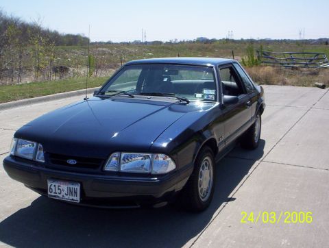 1991 Ford Mustang - A dark blue 1991 Ford Mustang coupe is parked on a concrete surface with a grassy field in the background.