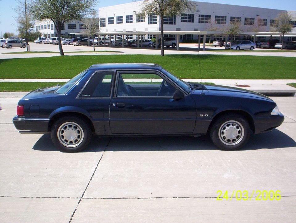 Dark blue 1991 Ford Mustang coupe parked on concrete, side view. "5.0" badge visible on fender
