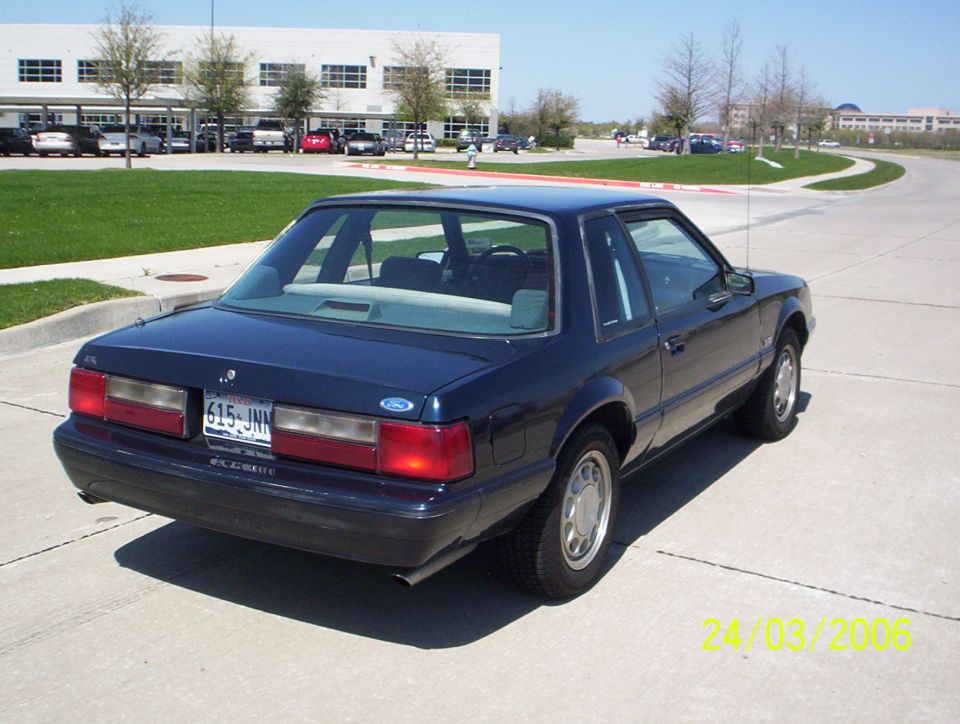 dark blue coupe parked on pavement, building and trees in background