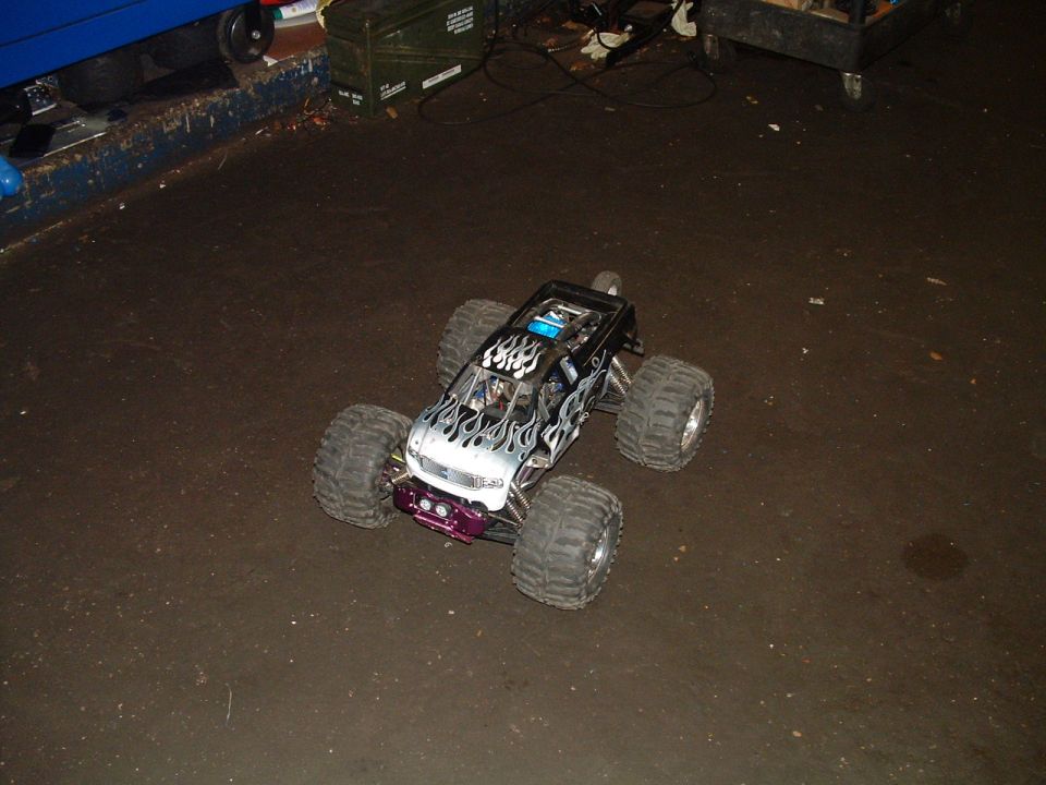 RC monster truck with flame decals and large tires on a dark floor