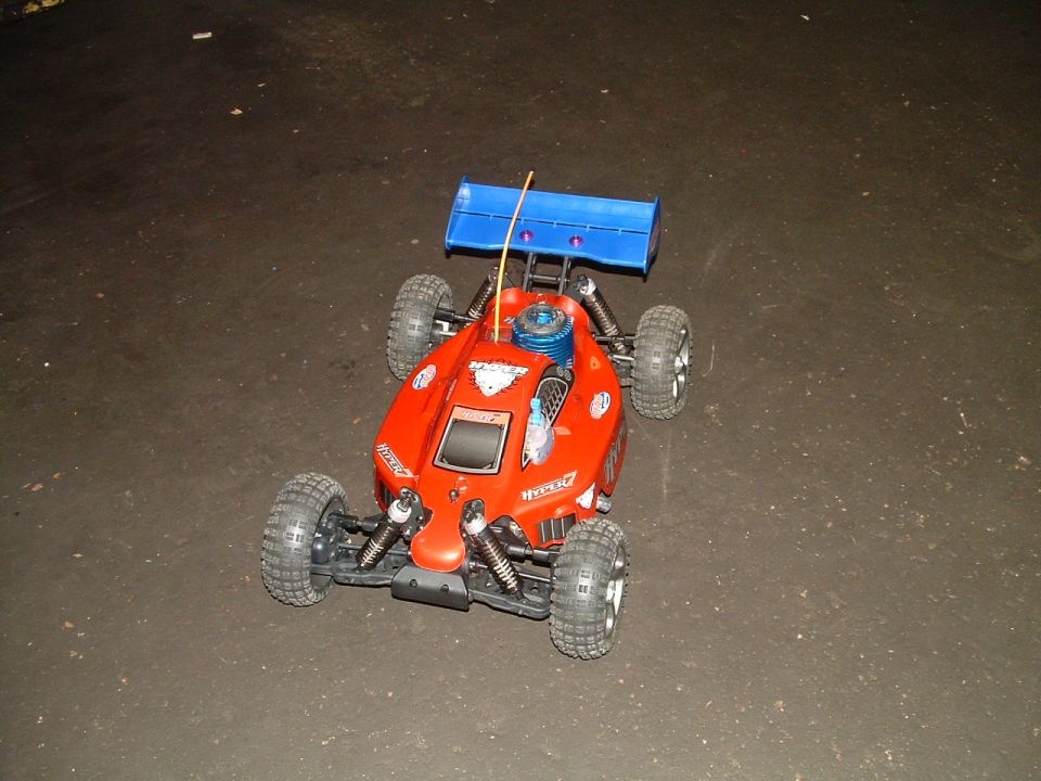Red remote control buggy with blue spoiler and visible engine on dark ground