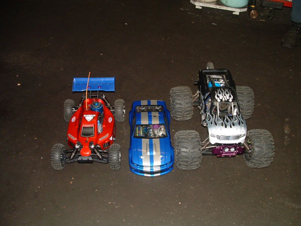 Three remote control cars lined up: a red buggy, a blue coupe, and a monster truck with flame decals