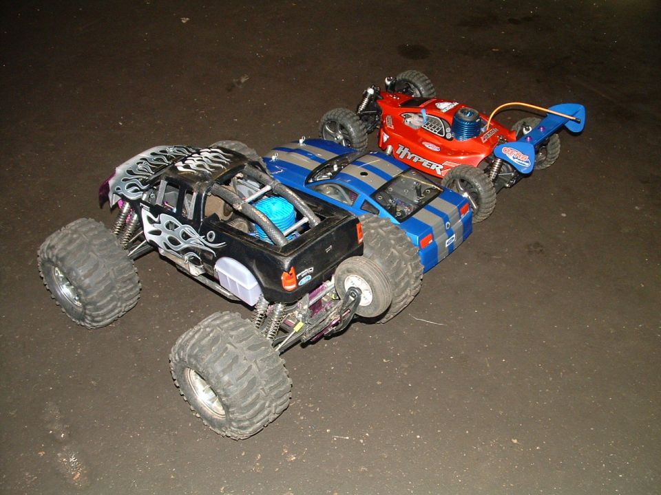 Three remote control vehicles lined up: a black monster truck with flame decals, a blue and gray striped car, and a red car with 'HYPER' text