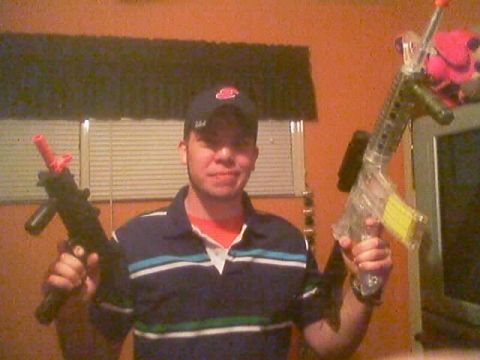 1985 Ford Bronco - Indoor snapshot of a person in a striped polo shirt and dark ball cap holding up two airsoft-style toy rifles, one black and one clear-bodi…