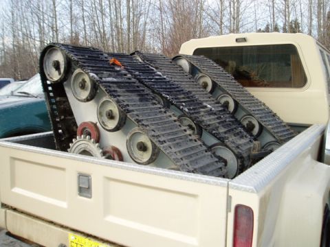 2000 Ford E350 - Snowmobile tracks are loaded into the bed of a cream-colored pickup truck, with another vehicle visible in the background.