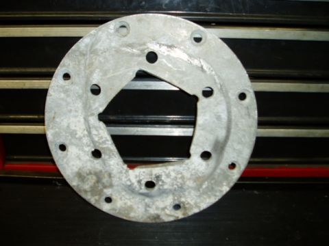 2000 Ford E350 - A metal flange with a central square opening and a ring of bolt holes sits on a black surface with horizontal lines.