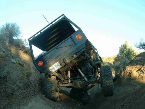 1986 Ford Bronco - This vehicle is navigating a challenging off-road trail, tilted at a precarious angle on a steep dirt incline.