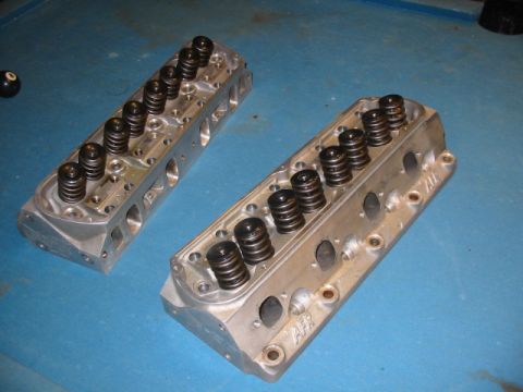 1985 Ford Crown Victoria LTD - Two aluminum engine cylinder heads with visible springs are displayed on a blue surface.