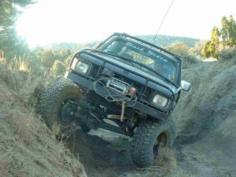 1986 Ford Bronco - A modified off-road vehicle navigates a challenging incline on a dry, dusty trail.