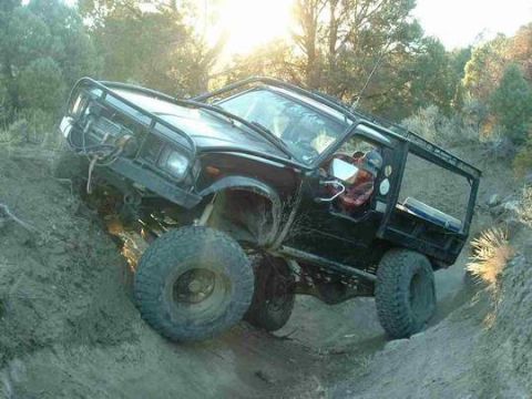 1986 Ford Bronco - This modified SUV is navigating a steep, muddy incline with a custom roll cage and off-road tires.
