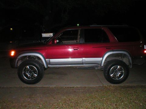 1996 Toyota 4Runner - A red 1996 Toyota 4Runner SUV is parked on a concrete surface at night, showing its lifted suspension and chrome wheels.