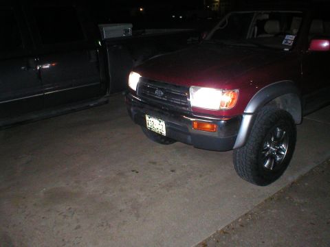 1996 Toyota 4Runner - Front corner view of a red 1996 Toyota 4Runner, parked next to a dark pickup truck at night.