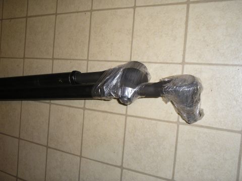1966 Ford Bronco - A black steel driveshaft lying on a beige tile floor, with its slip yoke and universal joint ends wrapped in clear plastic to keep them cle…