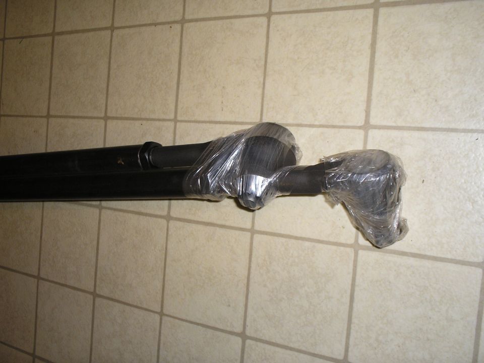 Black driveshaft on tile floor with slip yoke and U-joint ends wrapped in plastic