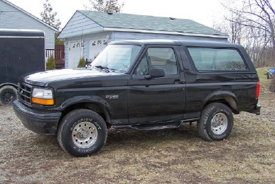 1994 Ford Bronco - This black Ford Bronco is parked outside a residential garage with a trailer nearby.