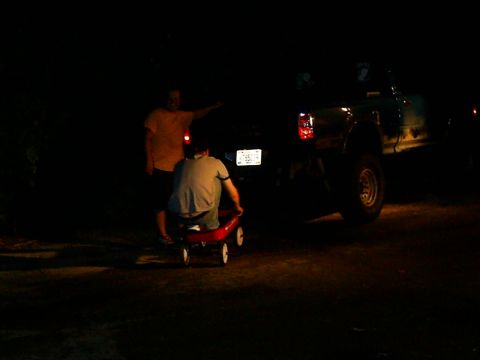 1985 Ford Bronco - Two people are near a truck at night, one is sitting in a red wagon.