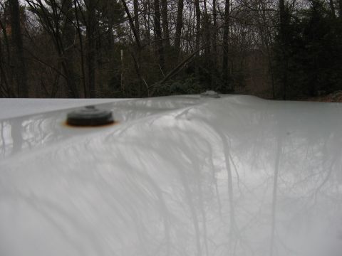 1995 Ford Bronco - The top of a white vehicle is visible, with two rusty mounting points and a wooded area behind it.