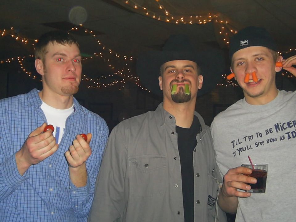 Three men with vegetables in their mouths and noses at a party