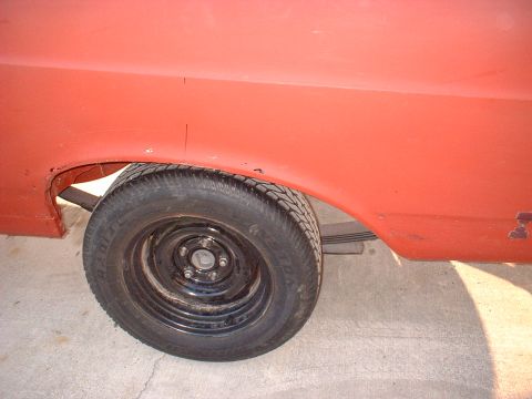 1967 Ford Ranchero - Close-up of the rear wheel well of a red pickup truck, showing the tire and suspension components.