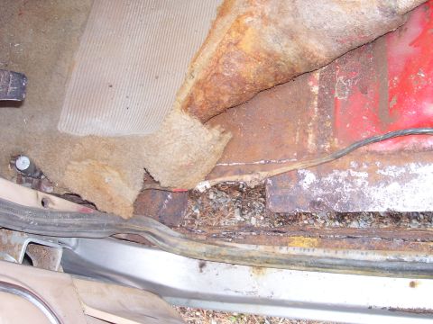 1984 Ford Bronco - Interior floor pan shows extensive rust damage and torn carpet, with a visible wire.