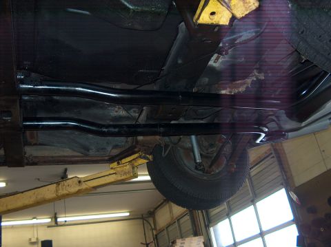 1979 Chevrolet Corvette - The underside of a vehicle is viewed from below while it is elevated on a lift, revealing its exhaust system and a tire.
