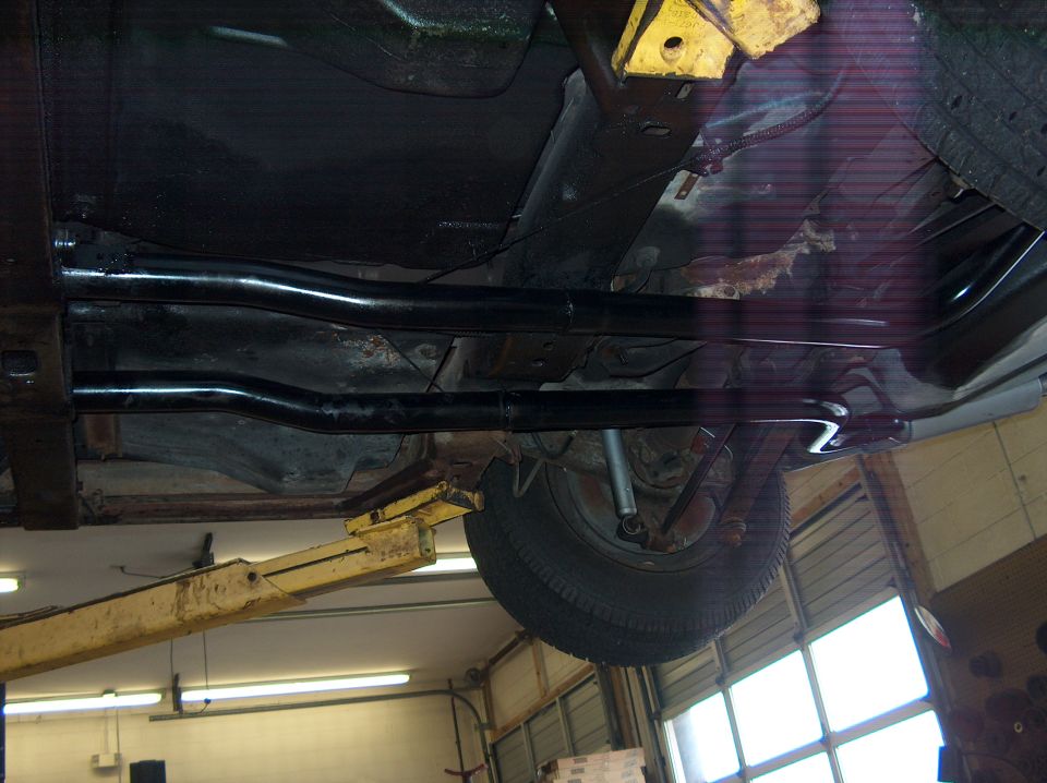 Undercarriage of a vehicle on a lift, showing exhaust pipes and a rear tire
