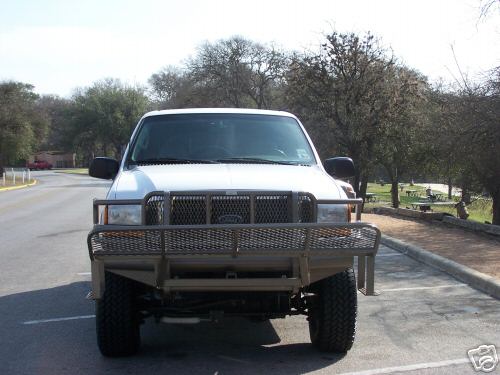 White lifted crew cab pickup with tan brush guard and expanded-metal front basket rack, front view