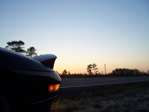 1994 Ford Probe - A car's rear is visible against a sunset sky, parked near a road.