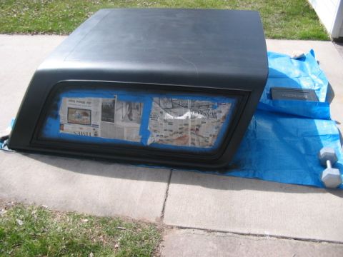 1991 Ford Bronco - A black car roof cap is prepared for painting, with newspaper covering the window area.