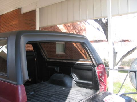 1991 Ford Bronco - Rear view of a red Ford Bronco showing its cargo area and black hardtop, parked outdoors.