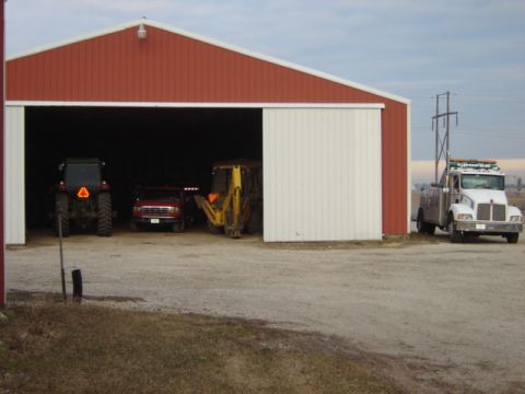1992 Ford Bronco - A white tow truck is parked next to a large red barn with an open bay.