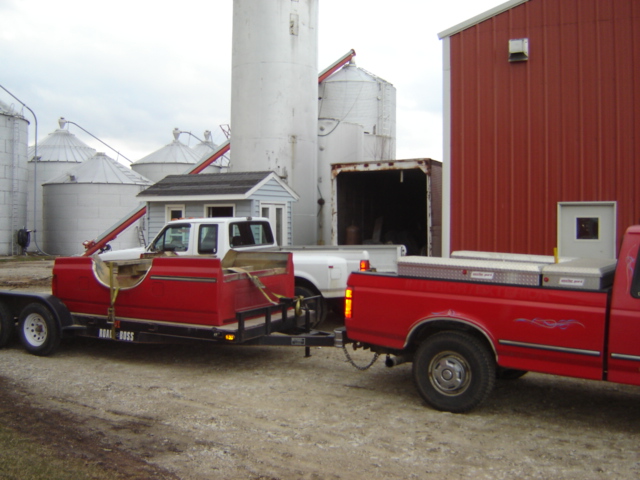 Red pickup truck towing a trailer with a red truck bed on it. Another red pickup is parked to the right
