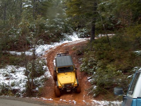 1993 Ford Bronco - A yellow Jeep Wrangler navigates a muddy trail in a snowy forest setting.
