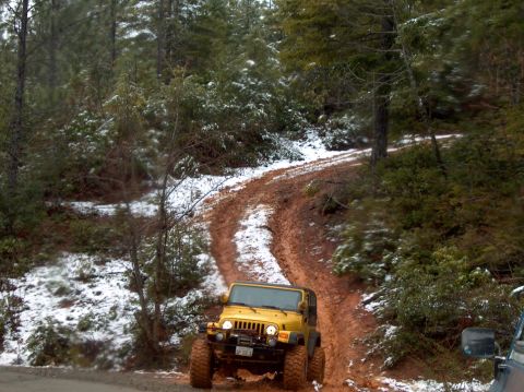 1993 Ford Bronco - A yellow Jeep navigates a muddy path with snow on the surrounding trees.