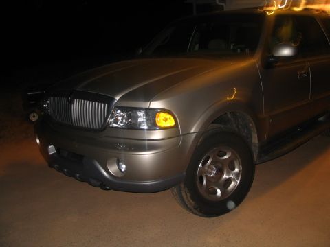 1989 Ford Bronco - Gold Lincoln Navigator SUV photographed at night, showing its front grille and headlight detail.